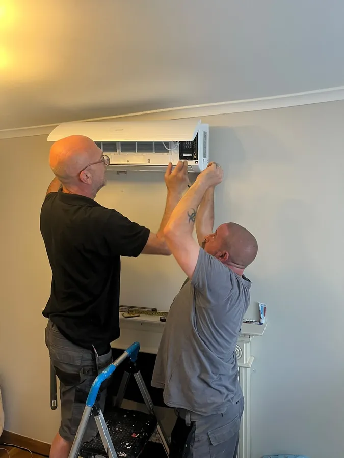 Two engineers servicing a wall-mounted indoor air conditioning unit