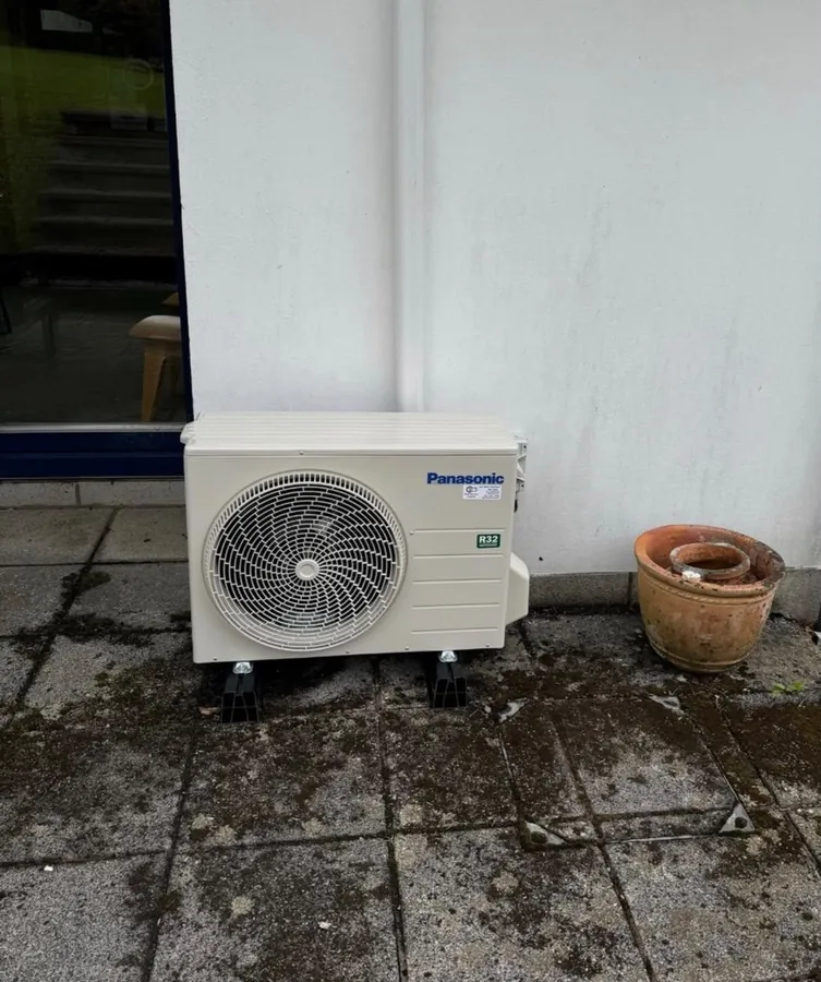 Panasonic outdoor air conditioning unit on a patio beside a rendered wall