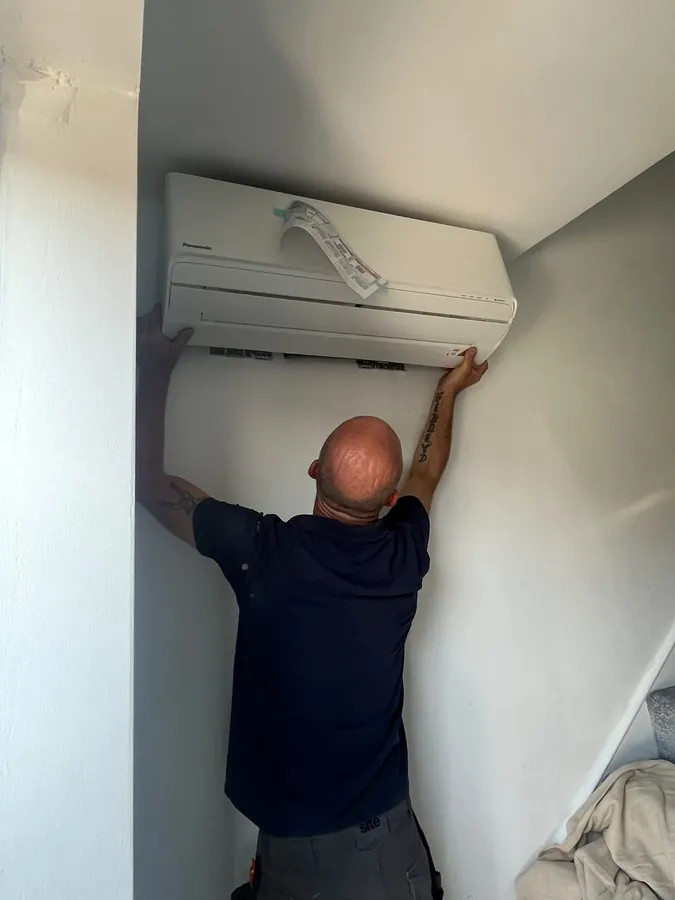 Engineer positioning a Panasonic indoor air conditioning unit on a wall