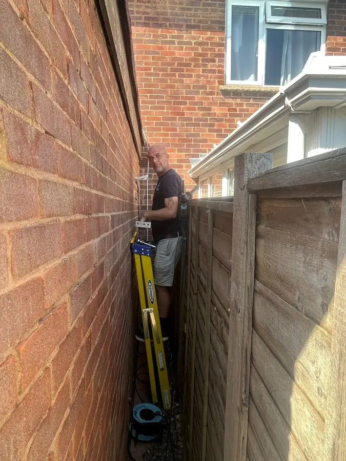 Engineer routing air con pipework in a narrow side passage of a Herefordshire home